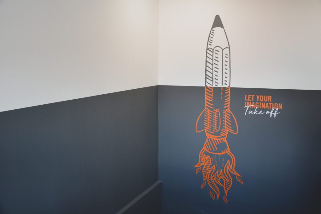 Grey and white wall with decal of rocket and words let your brand take off