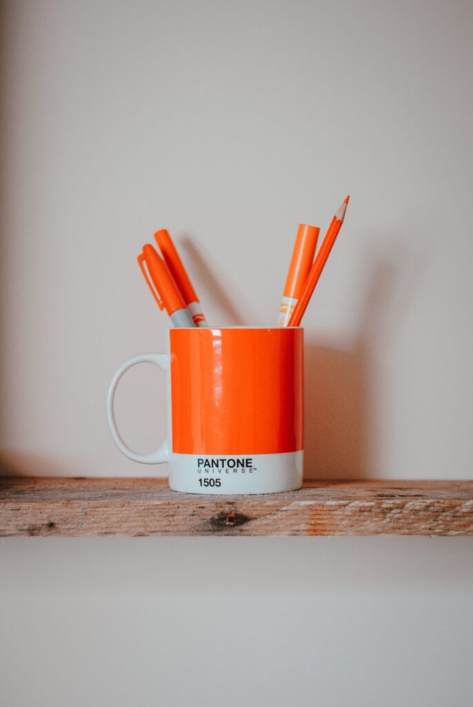 Orange mug with orange pens on a wooden shelf