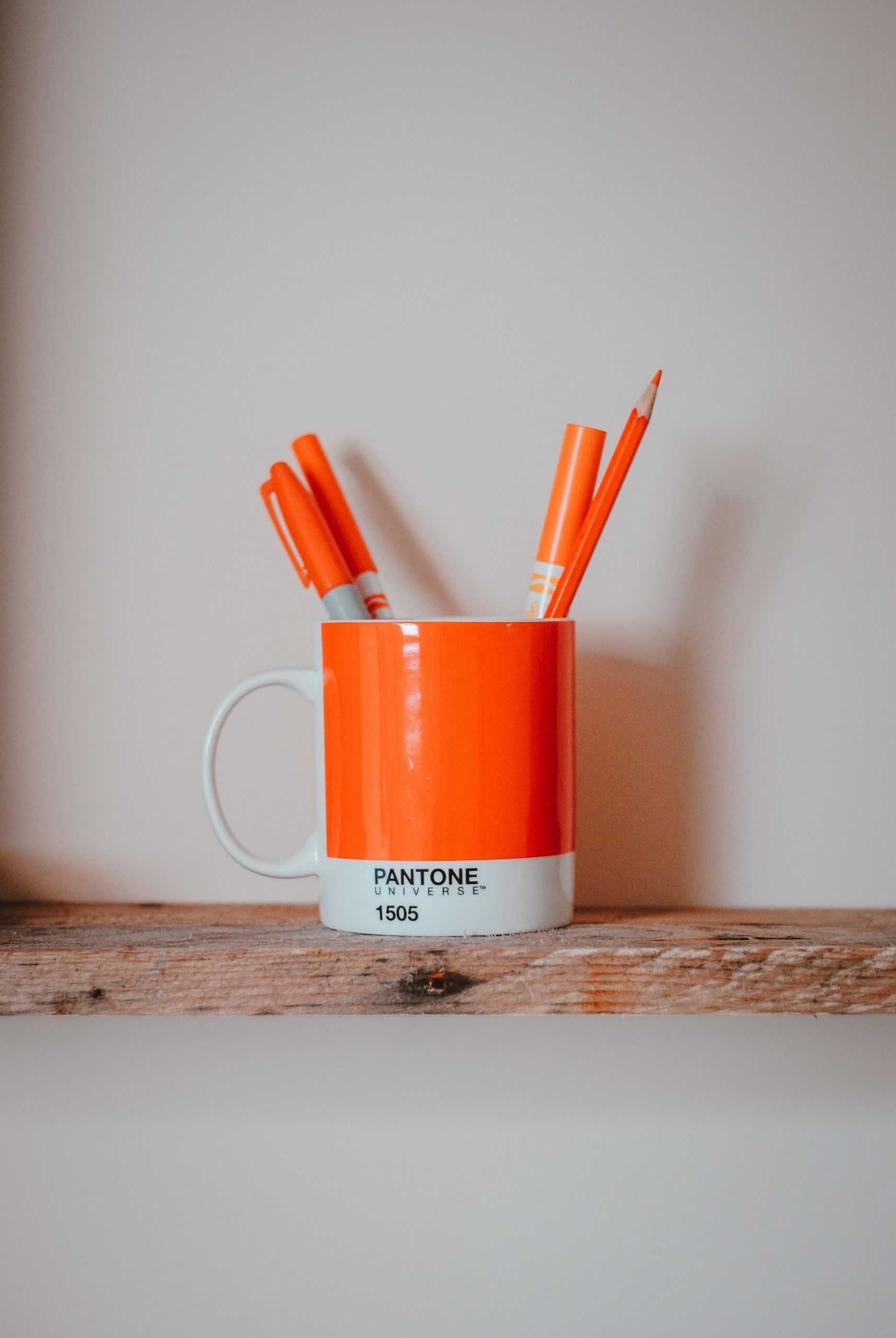 Orange mug with orange pens on a wooden shelf